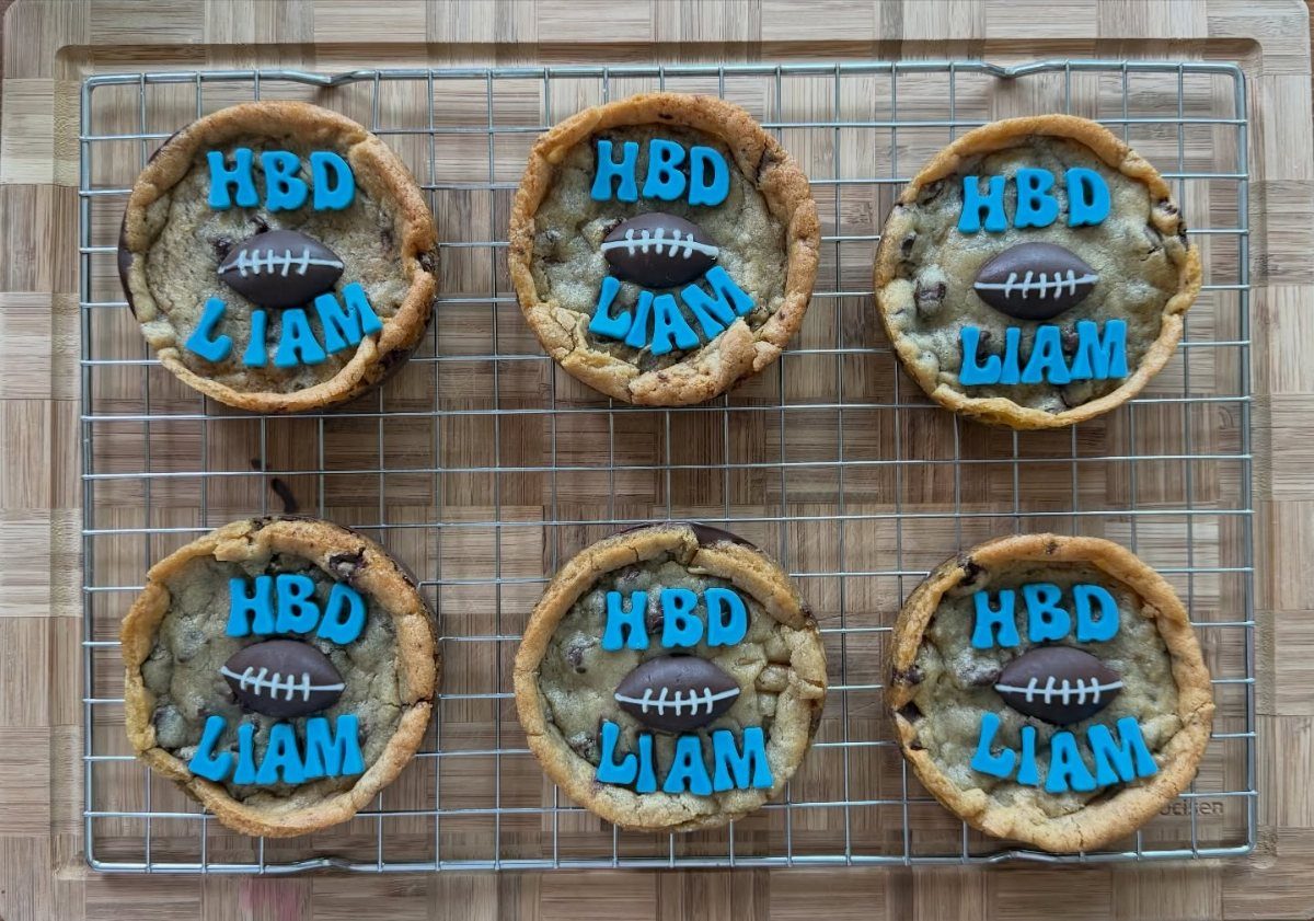 Chocolate chip cookies decorated with blue icing and chocolate footballs on a rack.