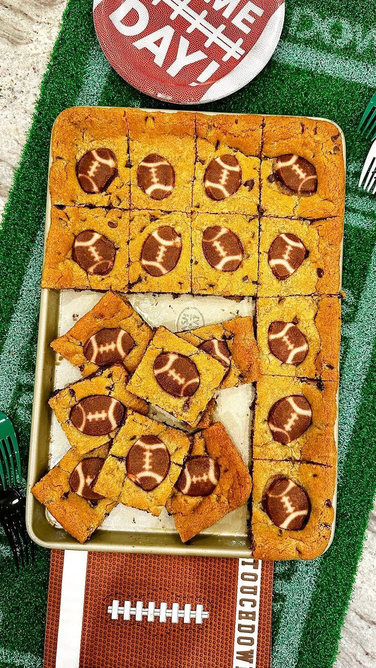 Chocolate chip cookies topped with chocolate football decorations on a baking sheet.