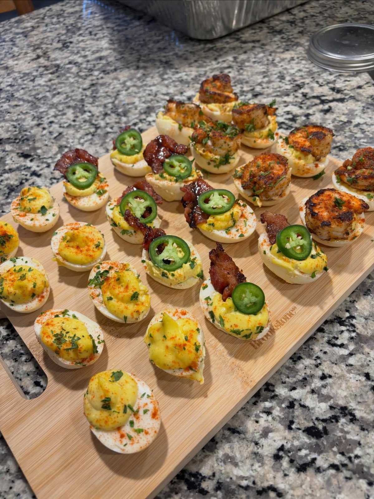 Deviled eggs topped with bacon, jalapeños, and herbs on a wooden serving board.