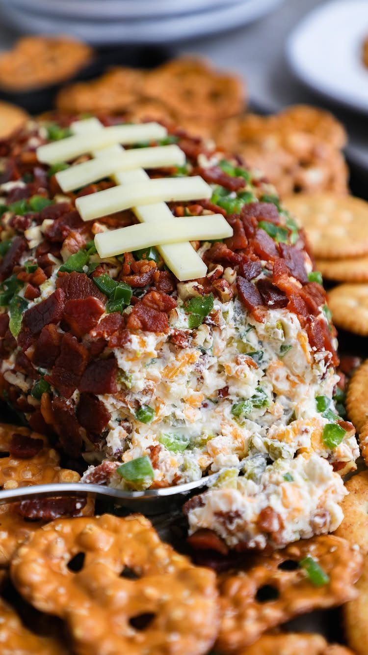 Football-shaped cheese ball with bacon and green onion coating served with pretzels.
