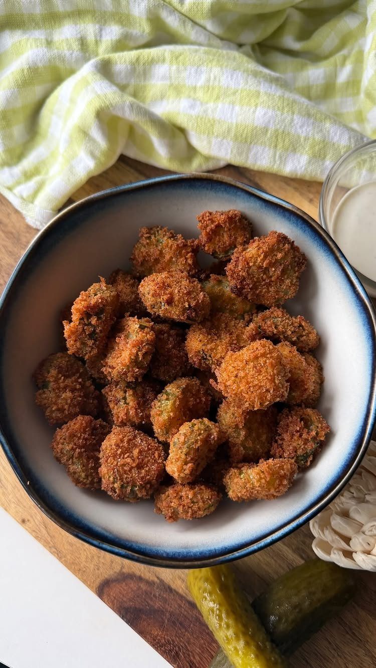Fried pickle slices in a blue bowl with dipping sauce and whole pickles.
