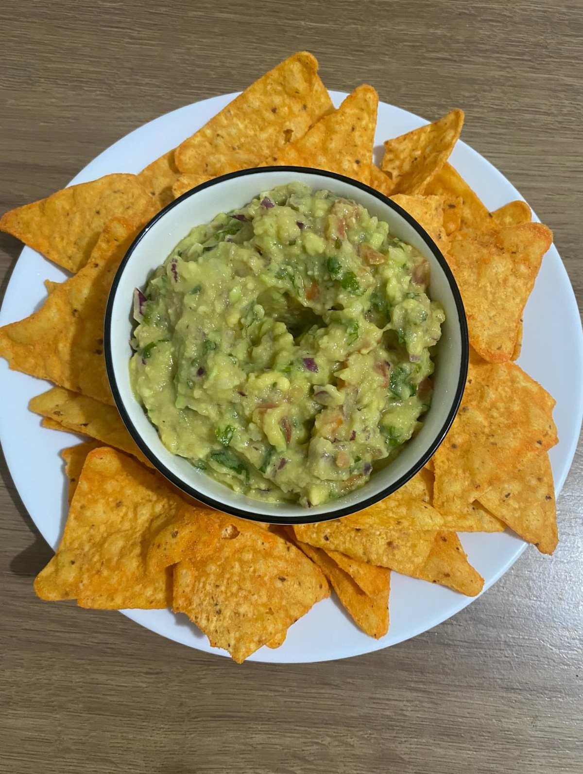Guacamole in a white bowl surrounded by orange tortilla chips on a plate