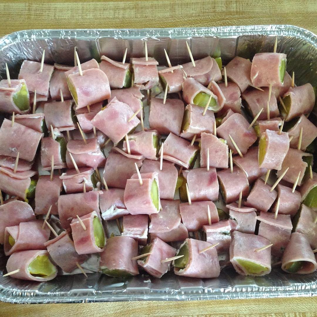 Ham and pickle roll-ups secured with toothpicks in an aluminum foil tray.