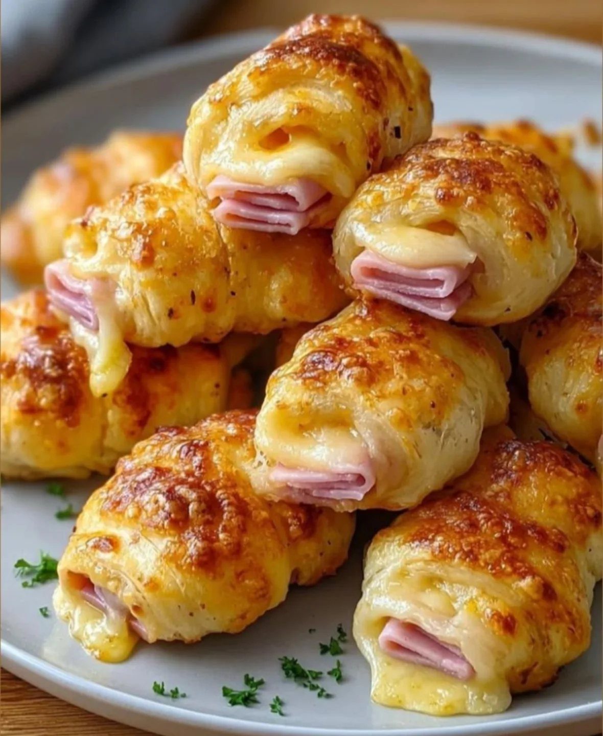 Golden-brown crescent rolls filled with melted cheese and ham on a white plate.