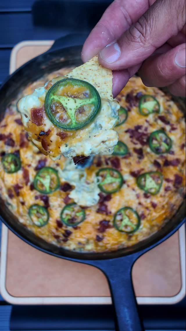 Creamy jalapeño popper dip in a cast-iron skillet with a chip scoop.