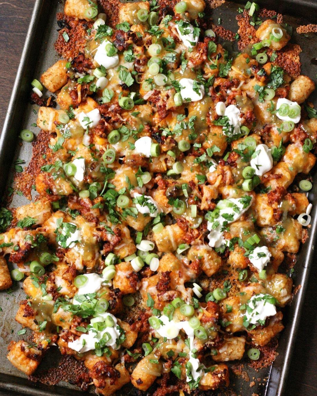 Loaded tater tot nachos with melted cheese, bacon, sour cream, and green onions.
