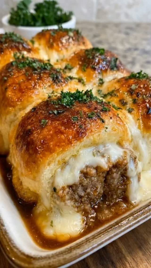 Meatball sliders with melted cheese and parsley in a white baking dish
