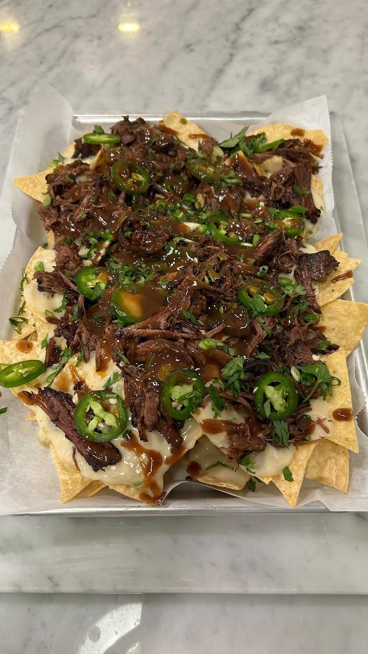 Nachos topped with shredded beef, melted cheese, jalapeños, and cilantro in a tray.