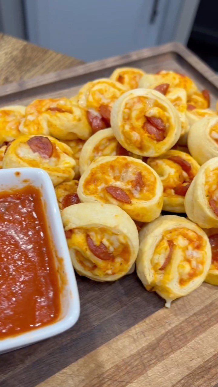 Pizza pinwheels with pepperoni and cheese on a wooden board with marinara sauce.