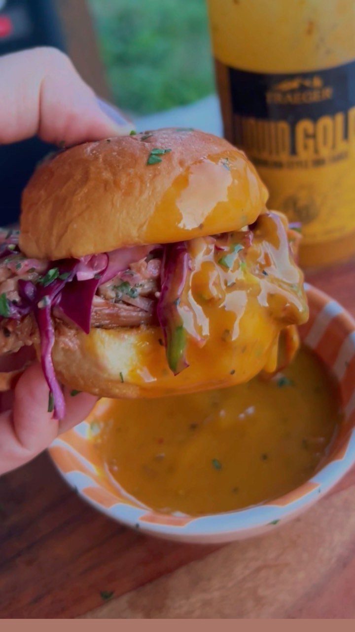 Pulled pork slider with purple cabbage and yellow sauce held over a dipping bowl.