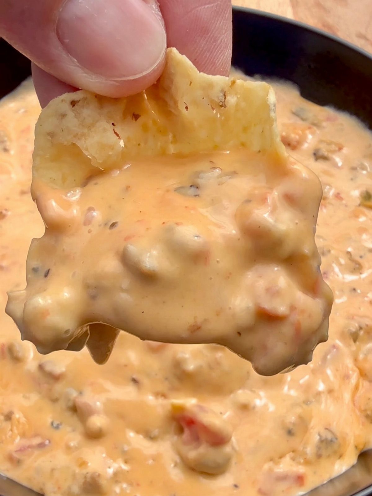 Tortilla chip scooped with creamy orange queso dip held over a pan