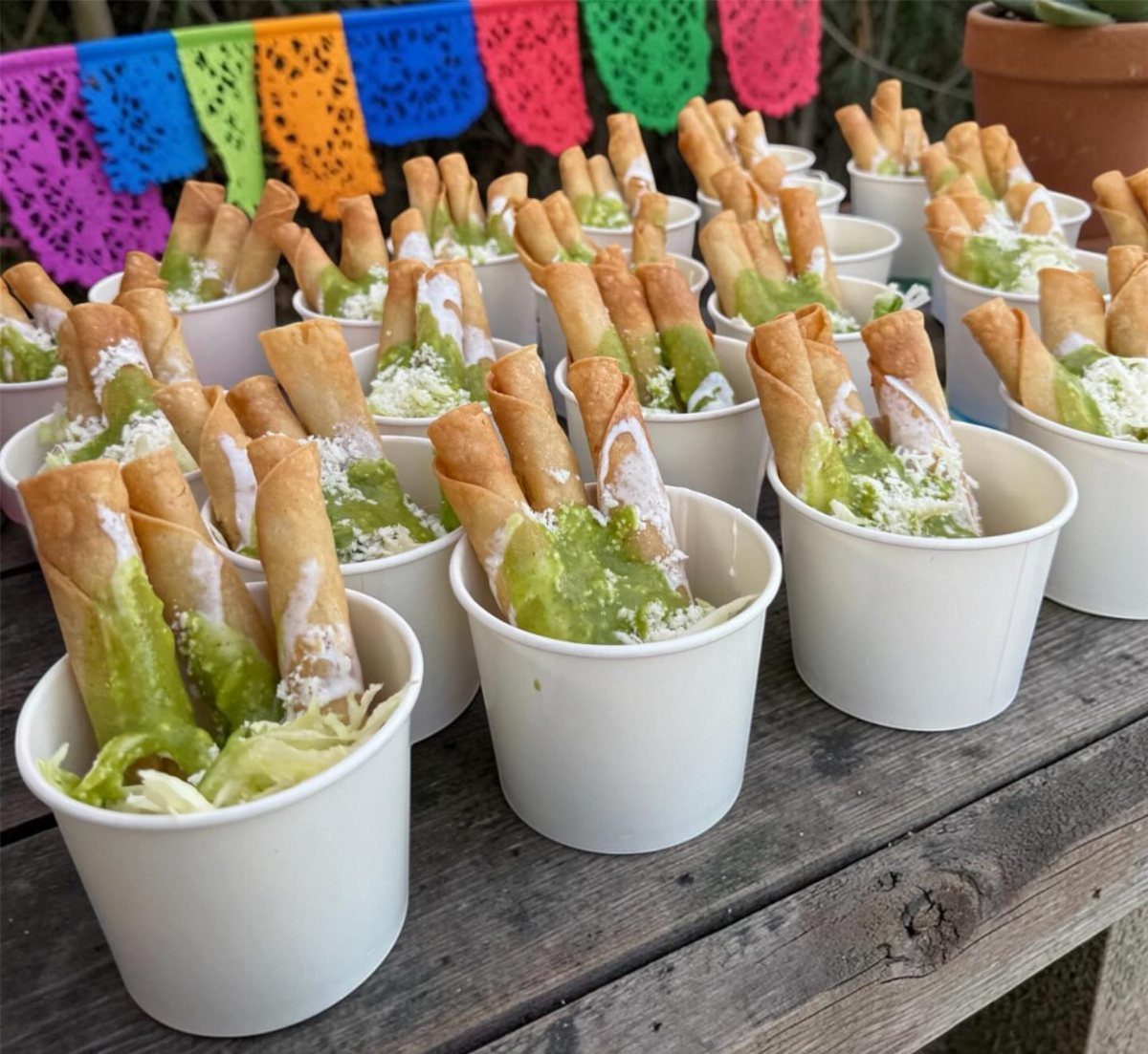 Crispy chicken taquitos with salsa verde and cotija cheese in white paper cups.