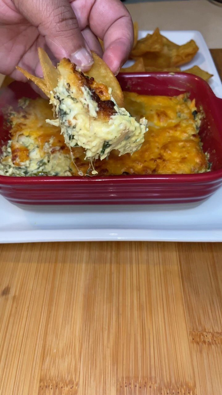 Spinach artichoke dip in a red dish with a chip scooping some out.