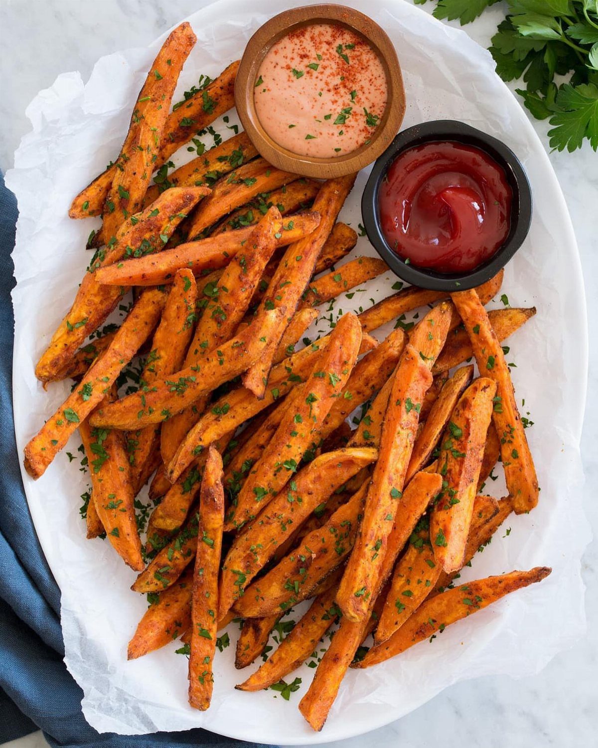 Sweet potato fries with herbs served with pink sauce and ketchup on parchment paper.