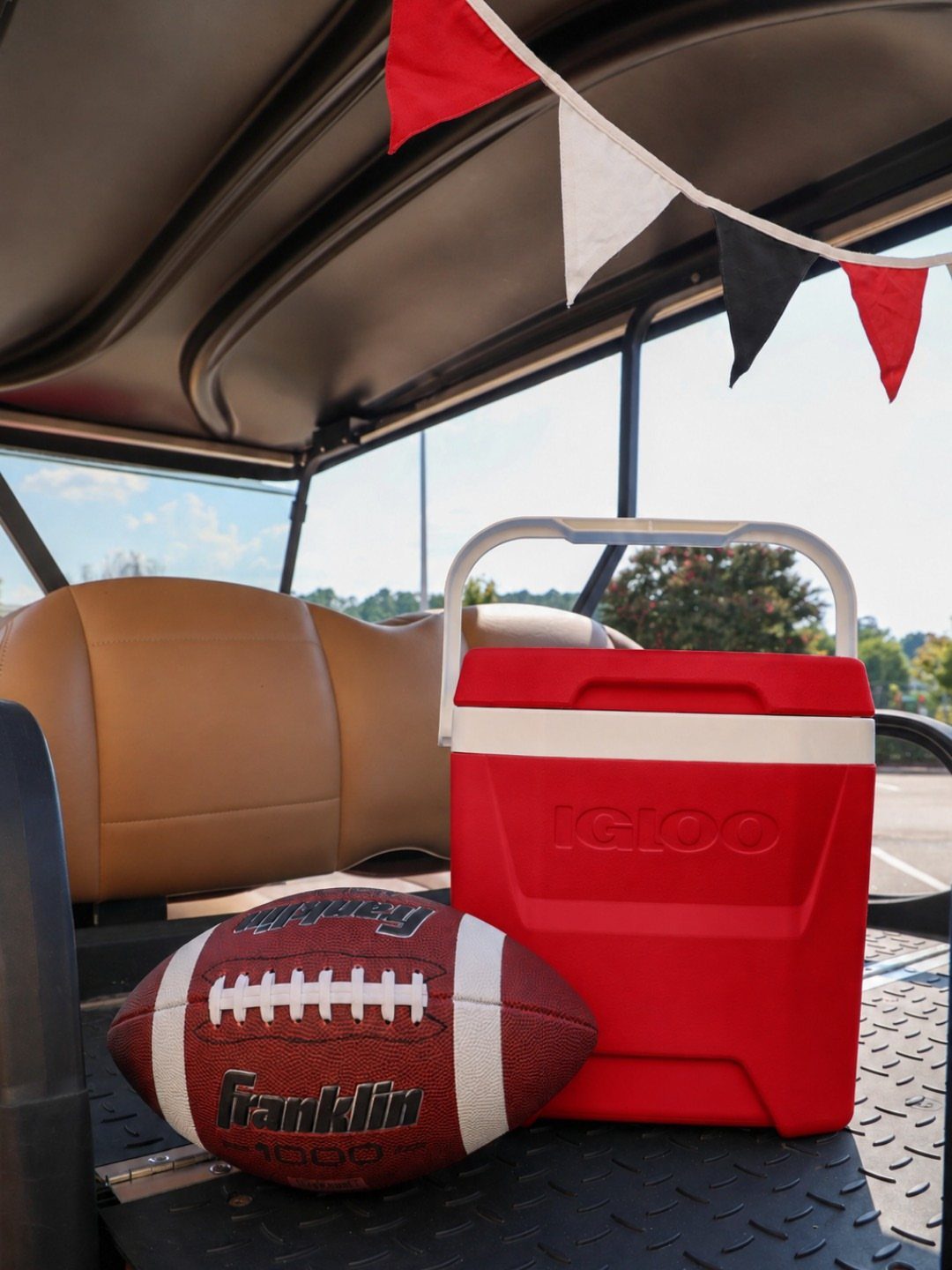 Red cooler and football on the floor of a golf cart with banners.
