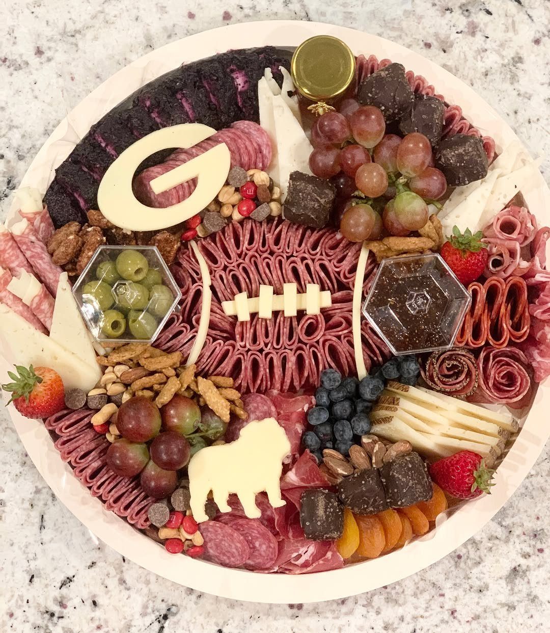 Football-themed charcuterie board with meat football, cheese shapes, fruits, and small jars.