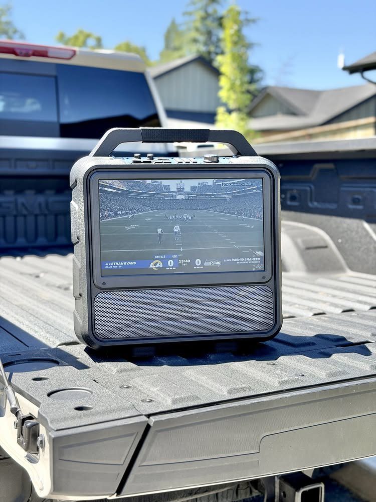 Portable TV and speaker displaying a football game in a truck bed