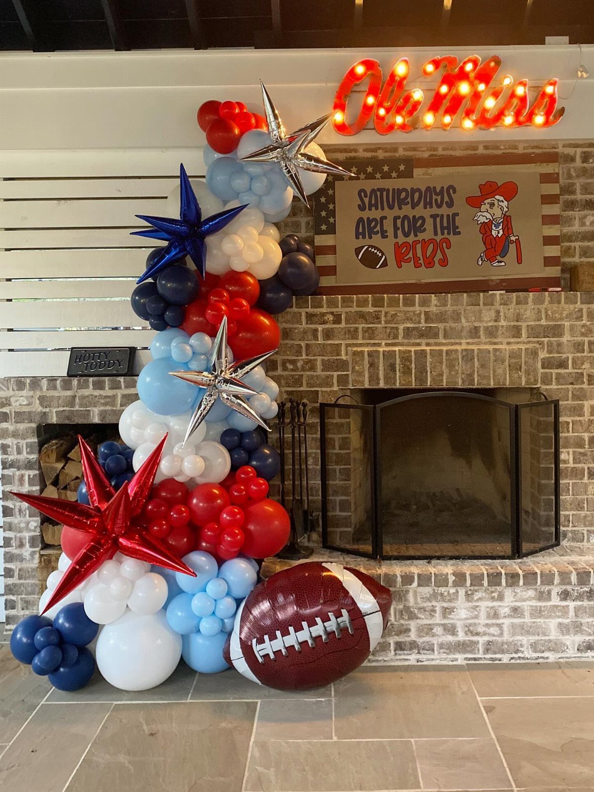 Balloon arch and inflatable football next to a brick fireplace for a tailgate party