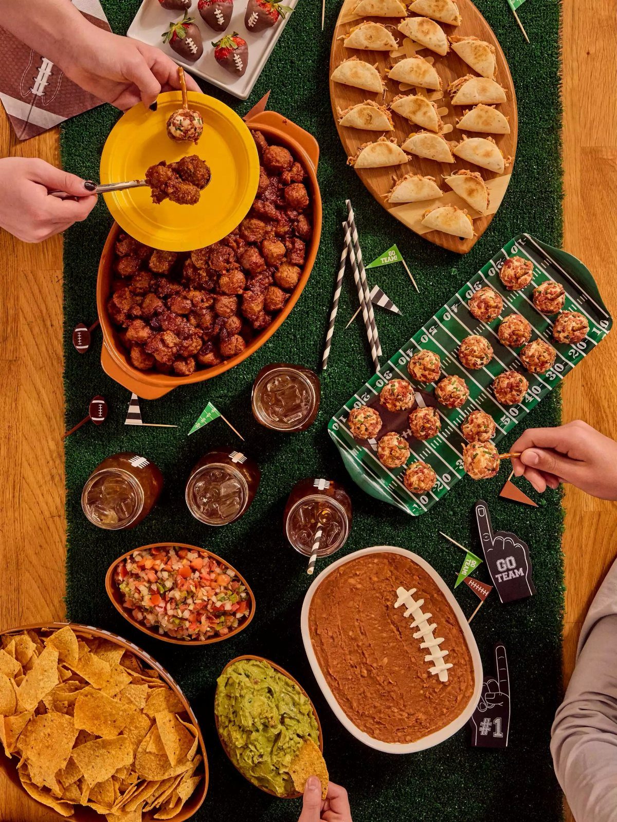 Assorted football-themed finger foods including meatballs, dips, and chips on green turf.