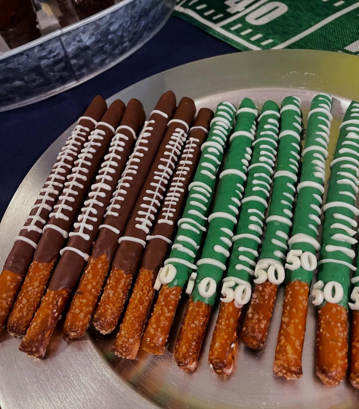 Chocolate and green candy-coated pretzel rods decorated like footballs on a silver platter.