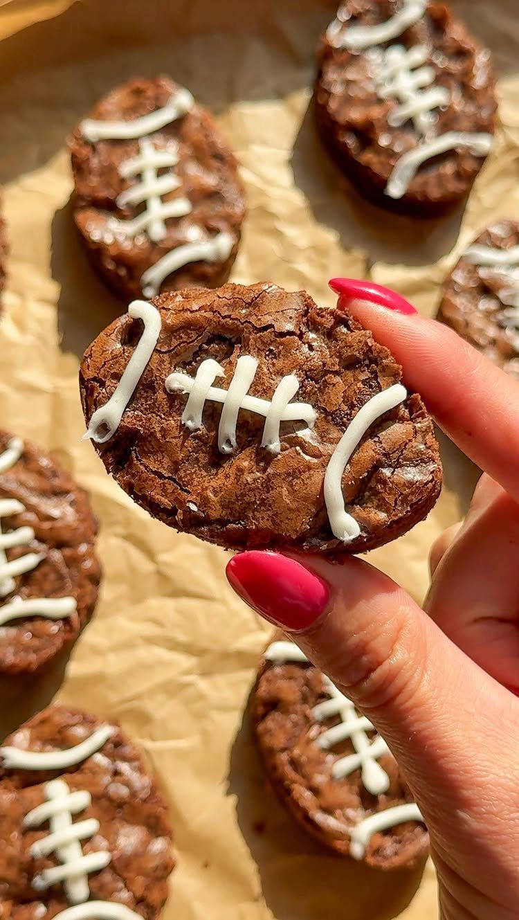 Football-shaped chocolate brownies with white icing laces on brown parchment paper.