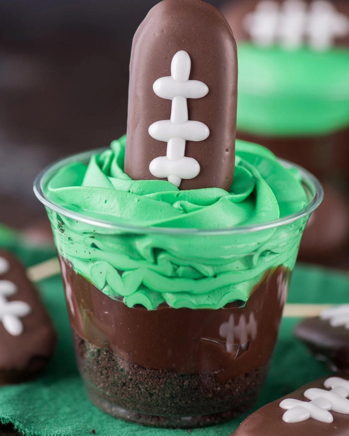 Layered chocolate and green frosting dessert cup topped with a chocolate football cookie.