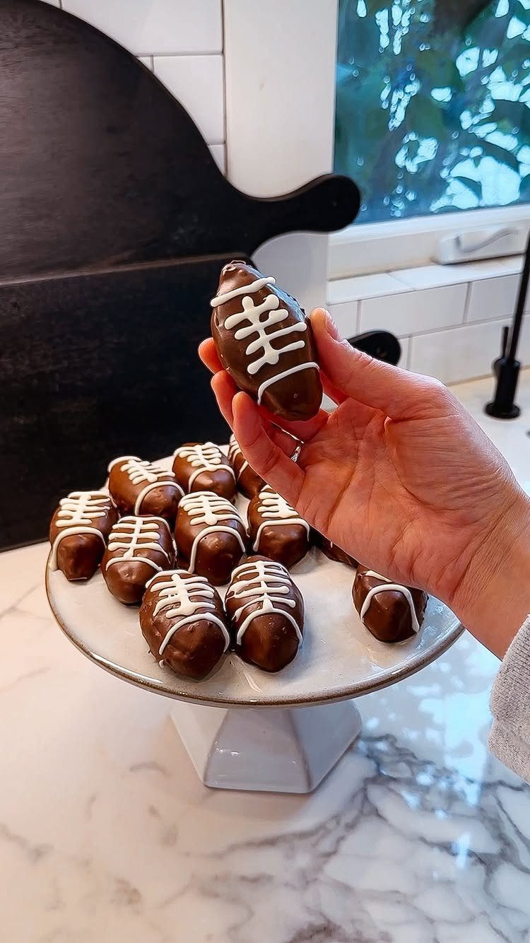 Chocolate football-shaped Oreo balls with white icing laces on a white cake stand.