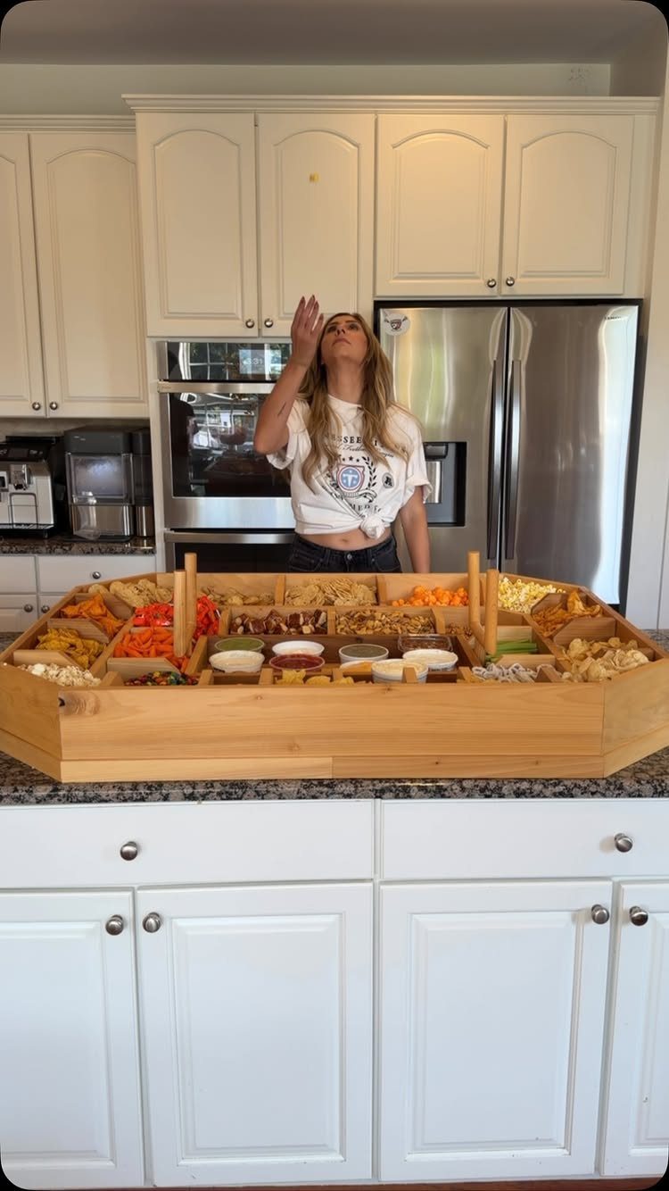 Large wooden snack board with appetizers on a kitchen counter with a woman.
