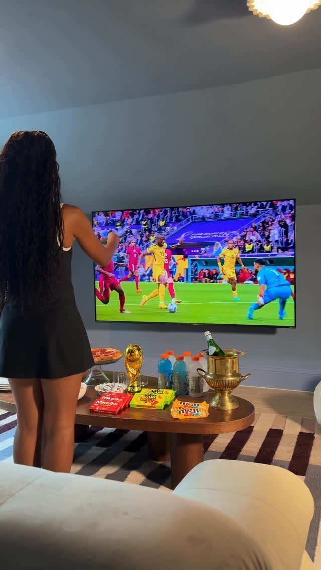 Woman watching a soccer match on a large television with snacks on a table