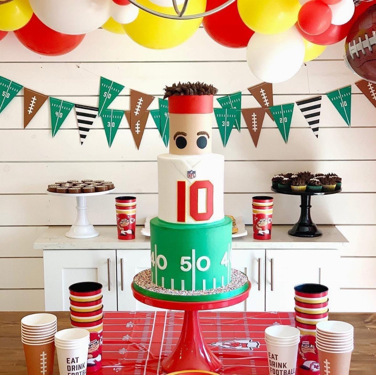 Football themed party table with a tiered cake, balloons, and themed decorations.