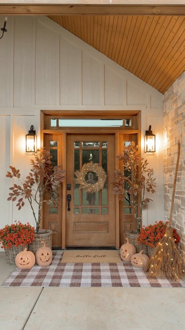 Decorated front porch with autumn foliage, pumpkins, a gold wreath, and glowing lanterns.