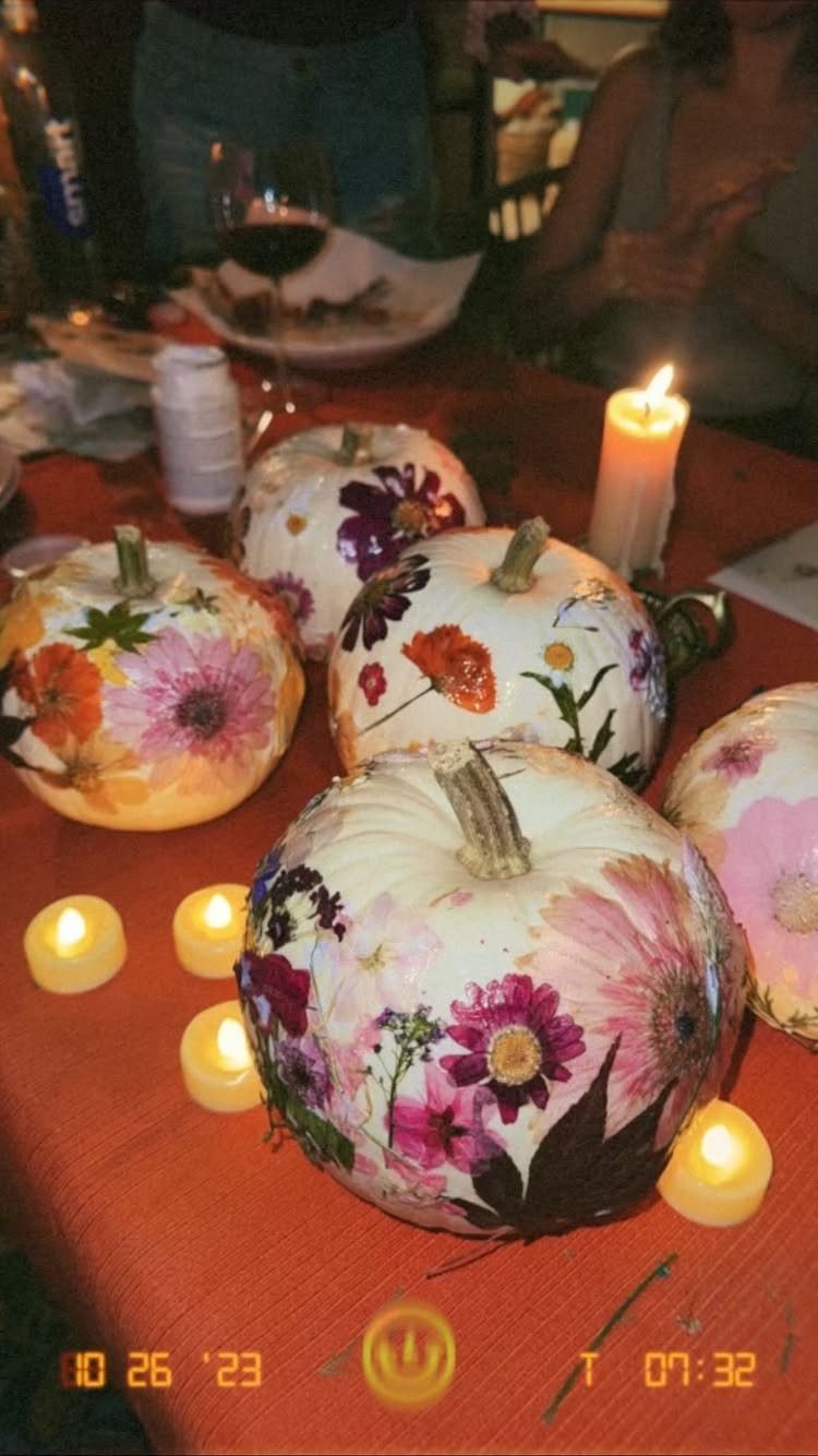 Floral decorated white pumpkins and lit candles on an orange tablecloth.