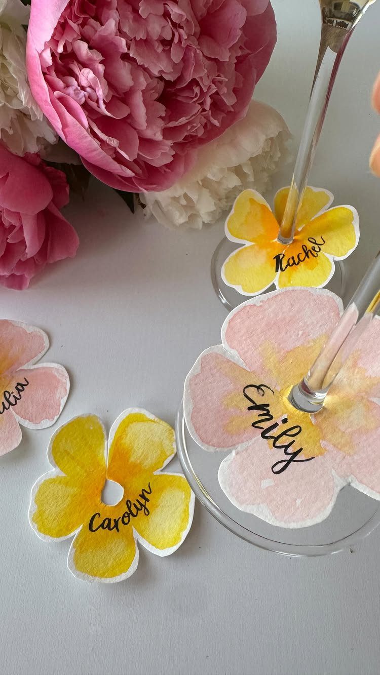 Flower-shaped watercolor drink markers with names placed under clear wine glass bases.