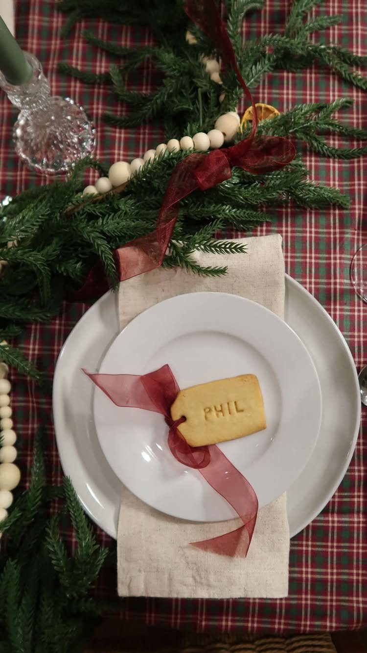 White plate with a name cookie and red ribbon on a plaid tablecloth.