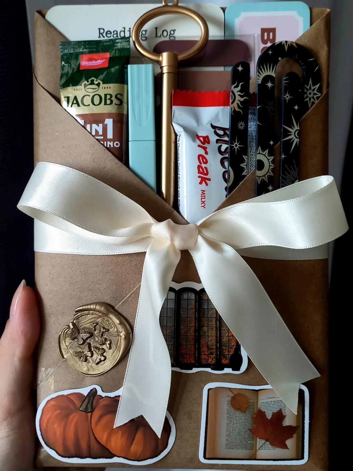 Brown paper gift bundle with white bow, coffee, snacks, and autumn stickers.