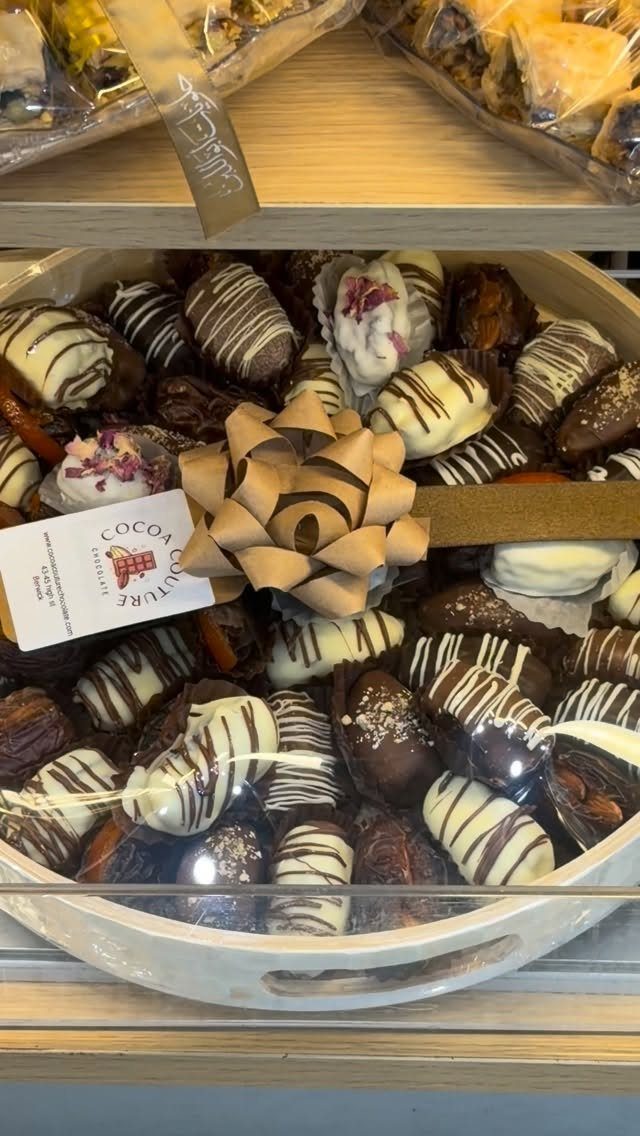 Chocolate covered dates in a white tray with a gold bow and label.