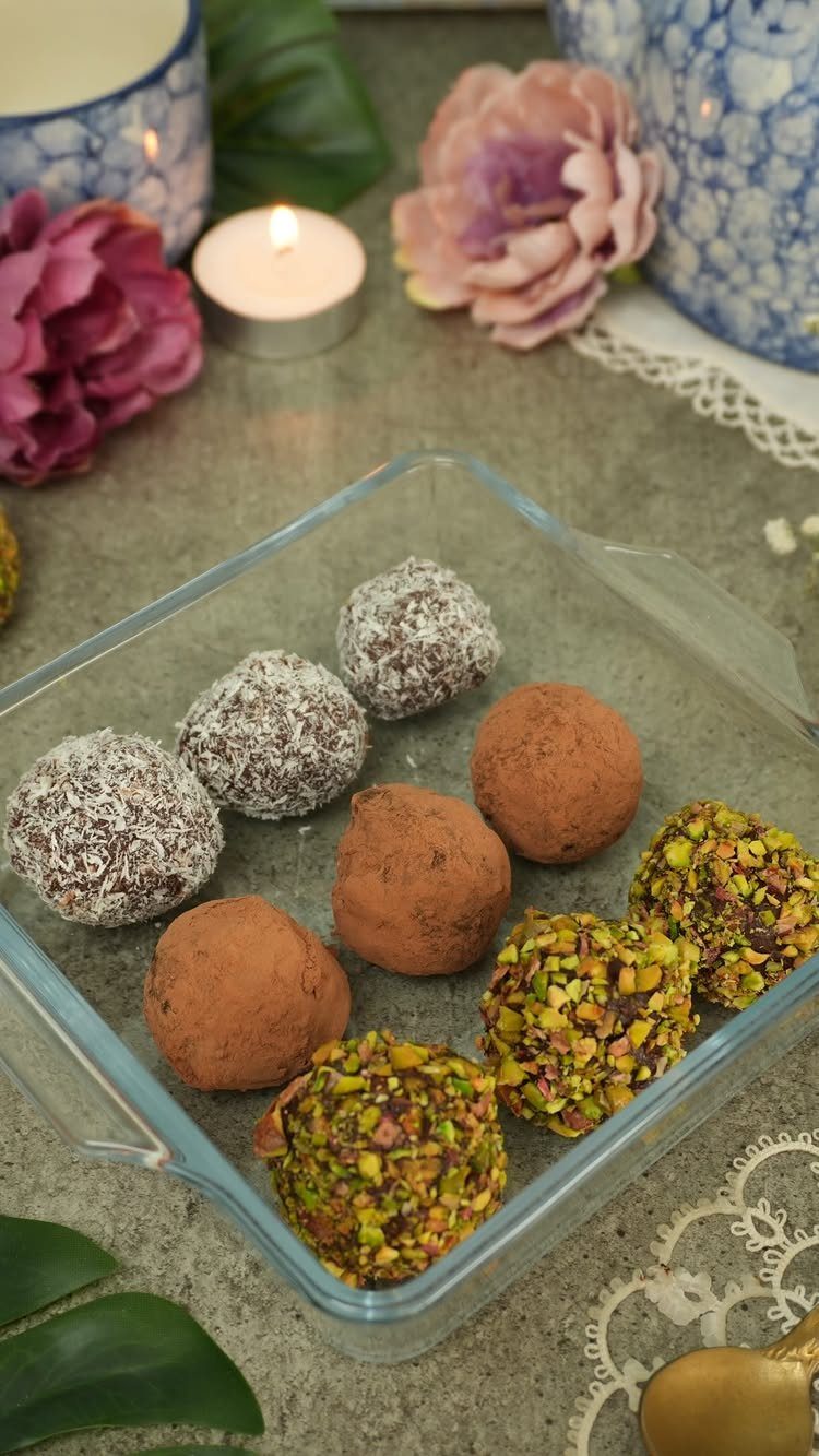 Assorted chocolate truffles in a glass dish with flowers and a candle.