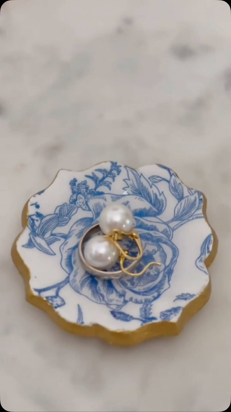 Small blue and white floral ceramic jewelry dish holding a pair of pearl earrings.