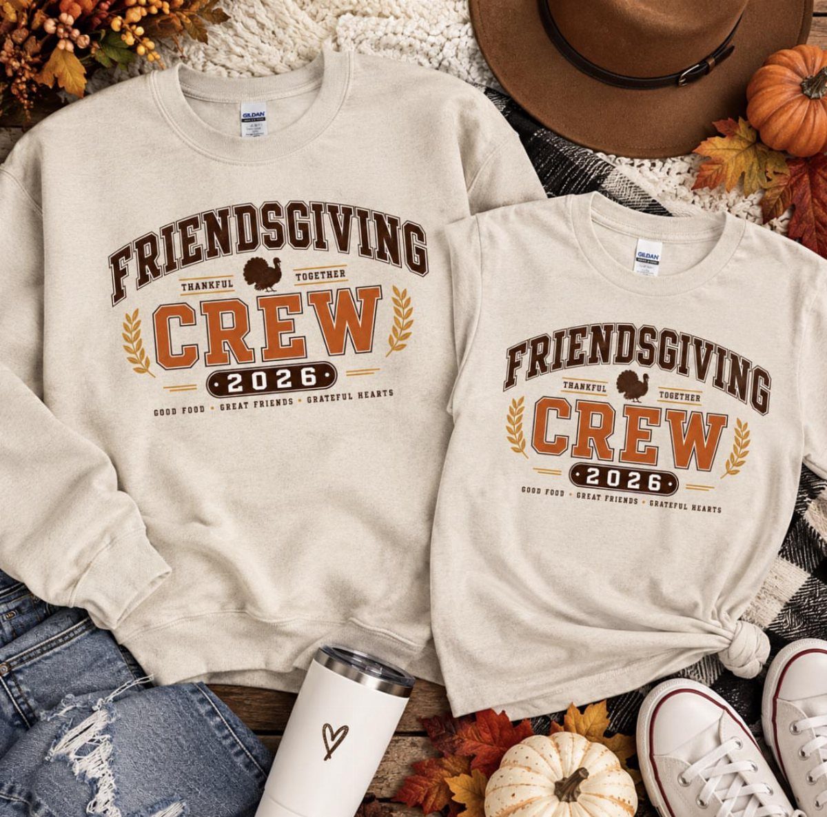 Two beige matching Friendsgiving Crew shirts surrounded by autumn leaves and pumpkins.