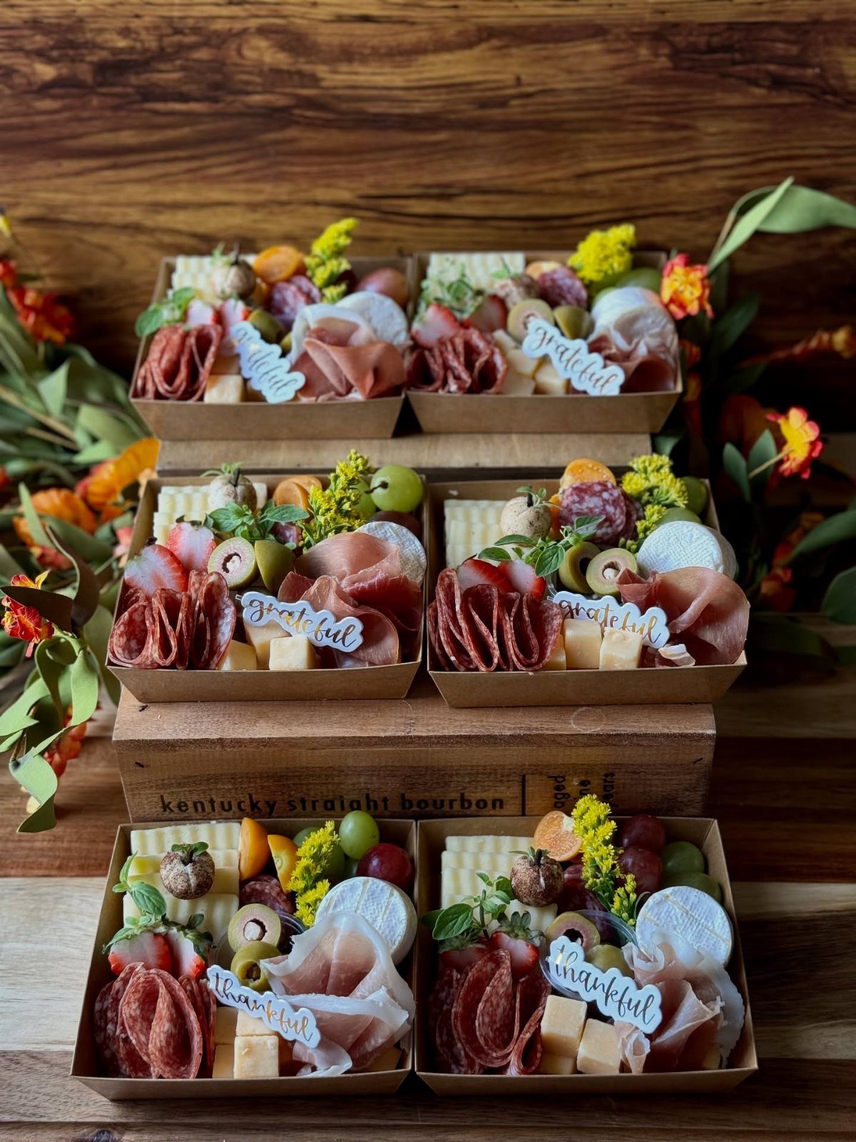 Charcuterie snack boxes with meats, cheeses, and fruits on a wooden background