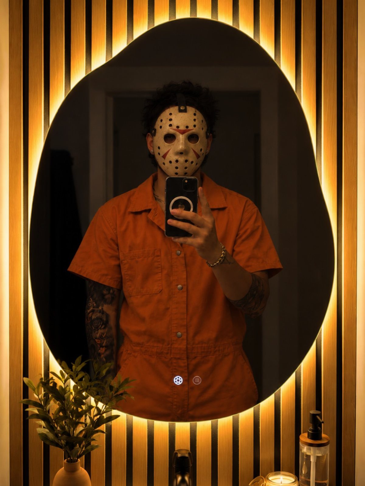 Person in a Jason Voorhees hockey mask and orange jumpsuit taking a mirror selfie.