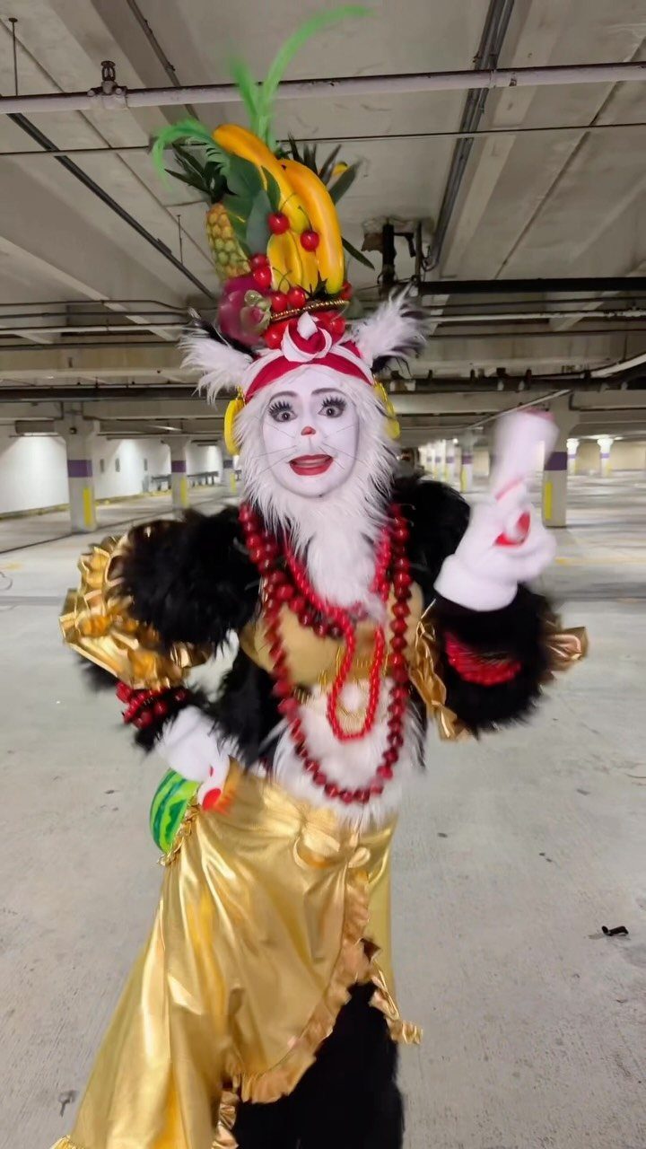 Person in a gold and white costume with fruit headpiece in a garage