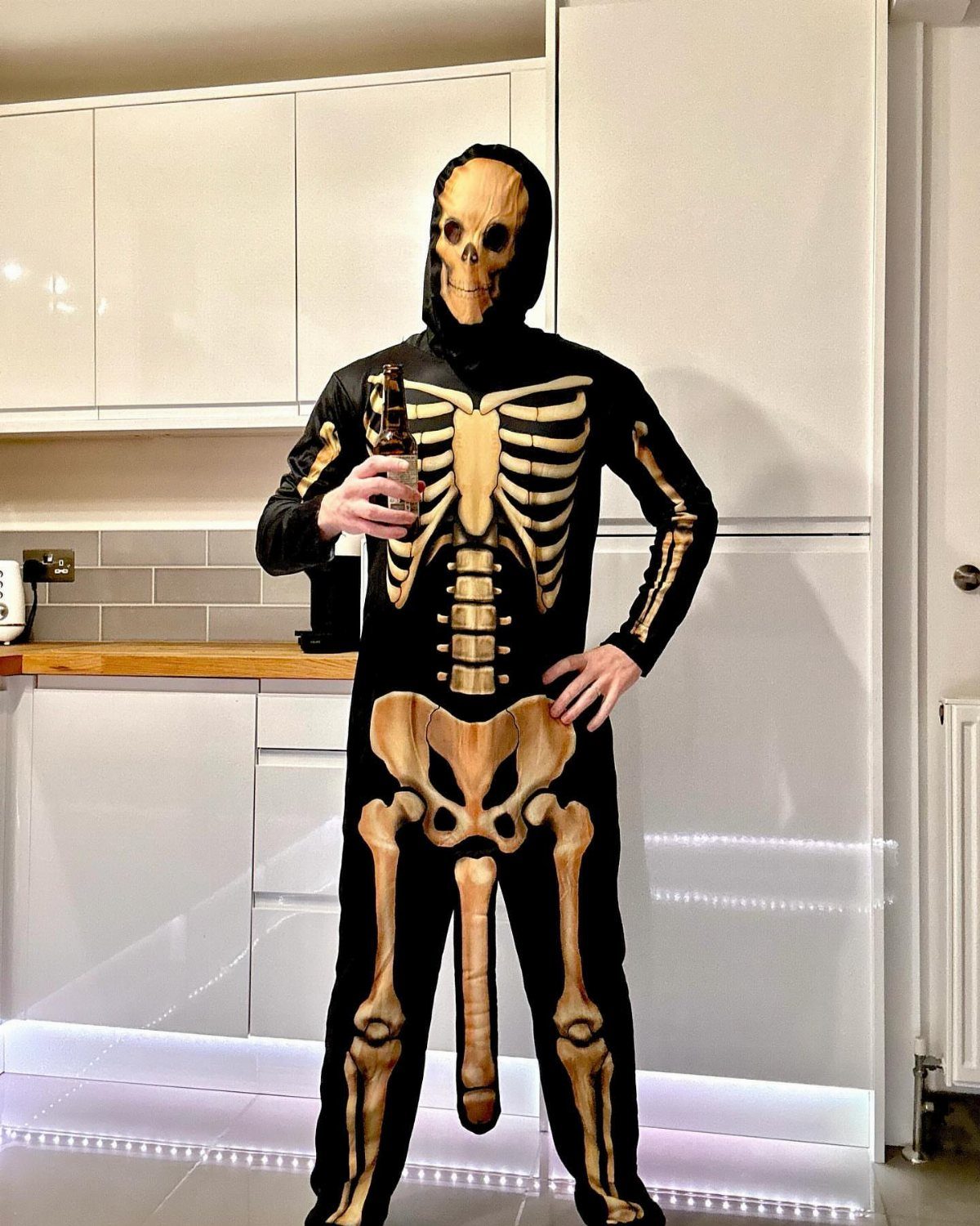 Person in a funny skeleton costume with a phallic bone standing in a kitchen