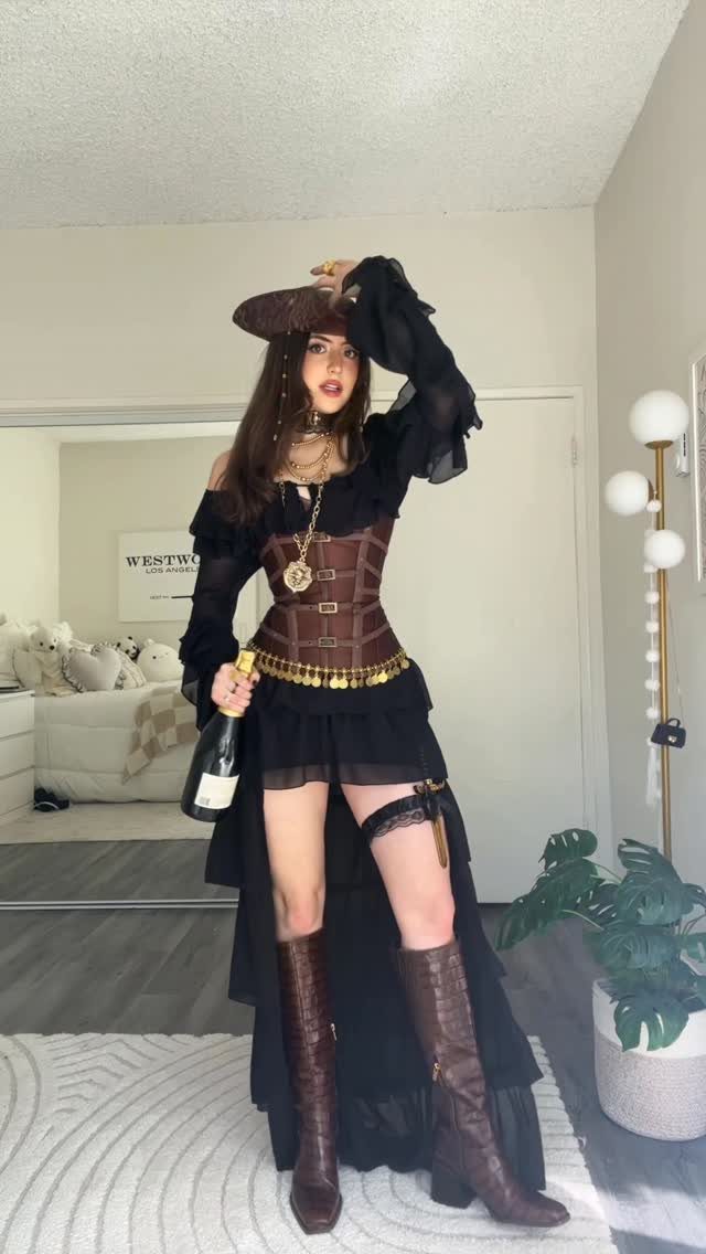 Woman wearing a pirate costume with a brown corset and tricorn hat posing indoors