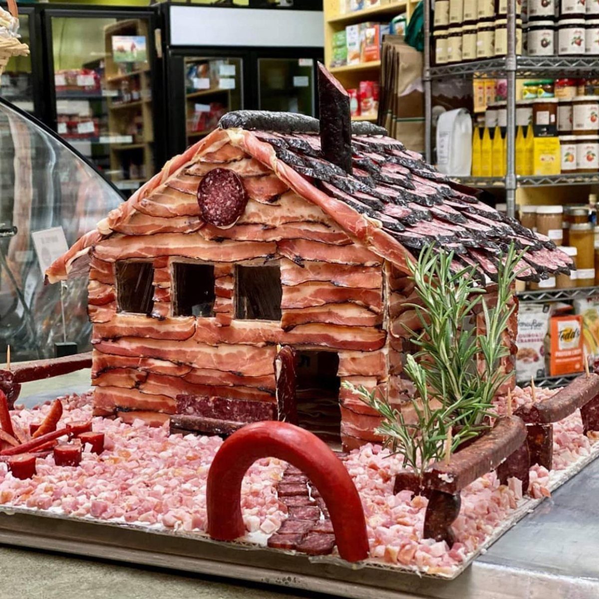 Miniature house made of bacon and salami with a sausage arch and rosemary shrubs.