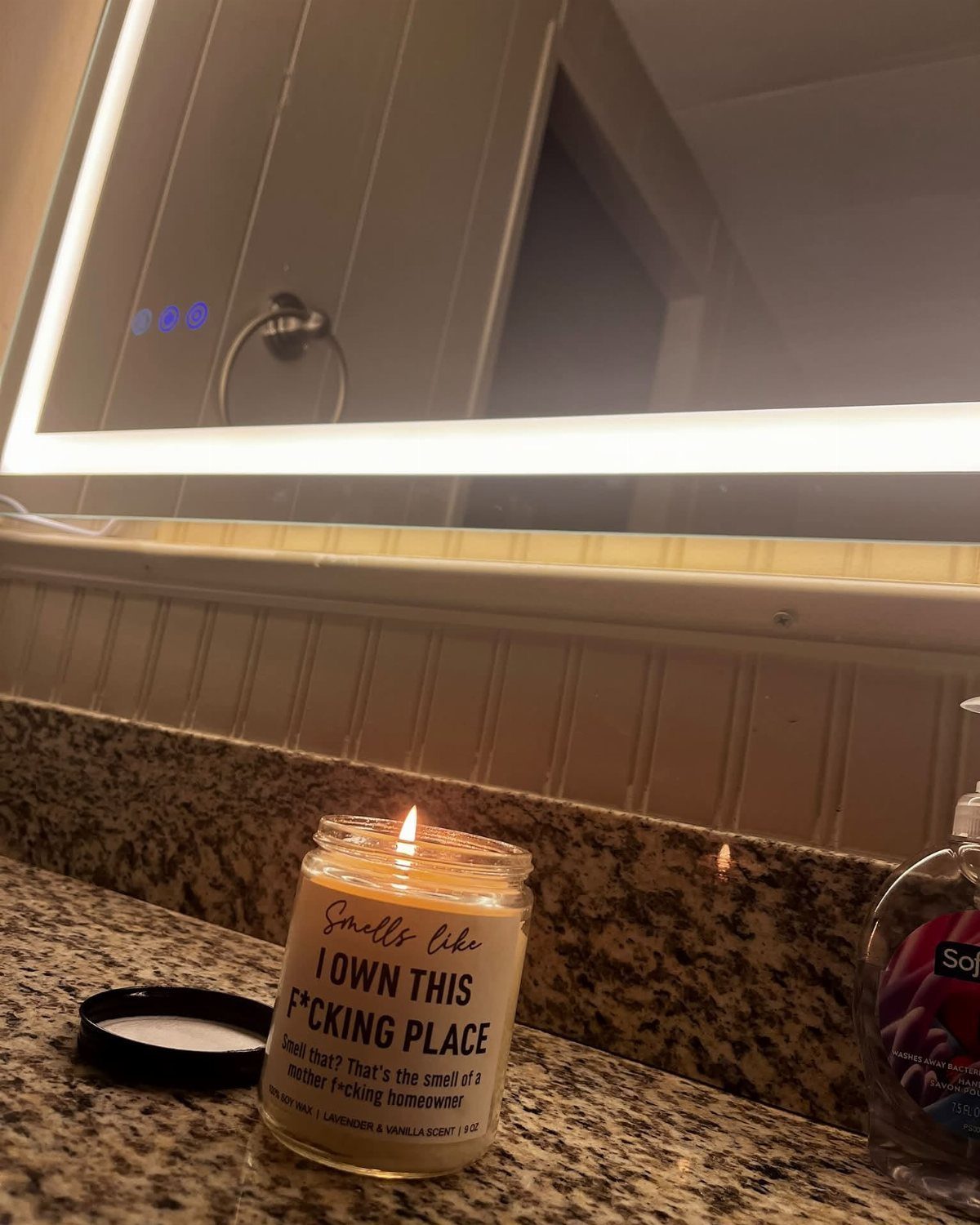 Lit candle with funny ownership label on a granite bathroom countertop