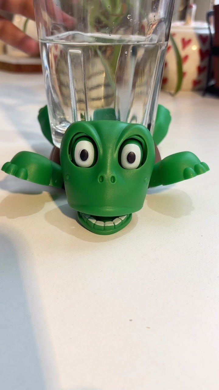 Green turtle-shaped glass holder holding a clear glass of water on white table