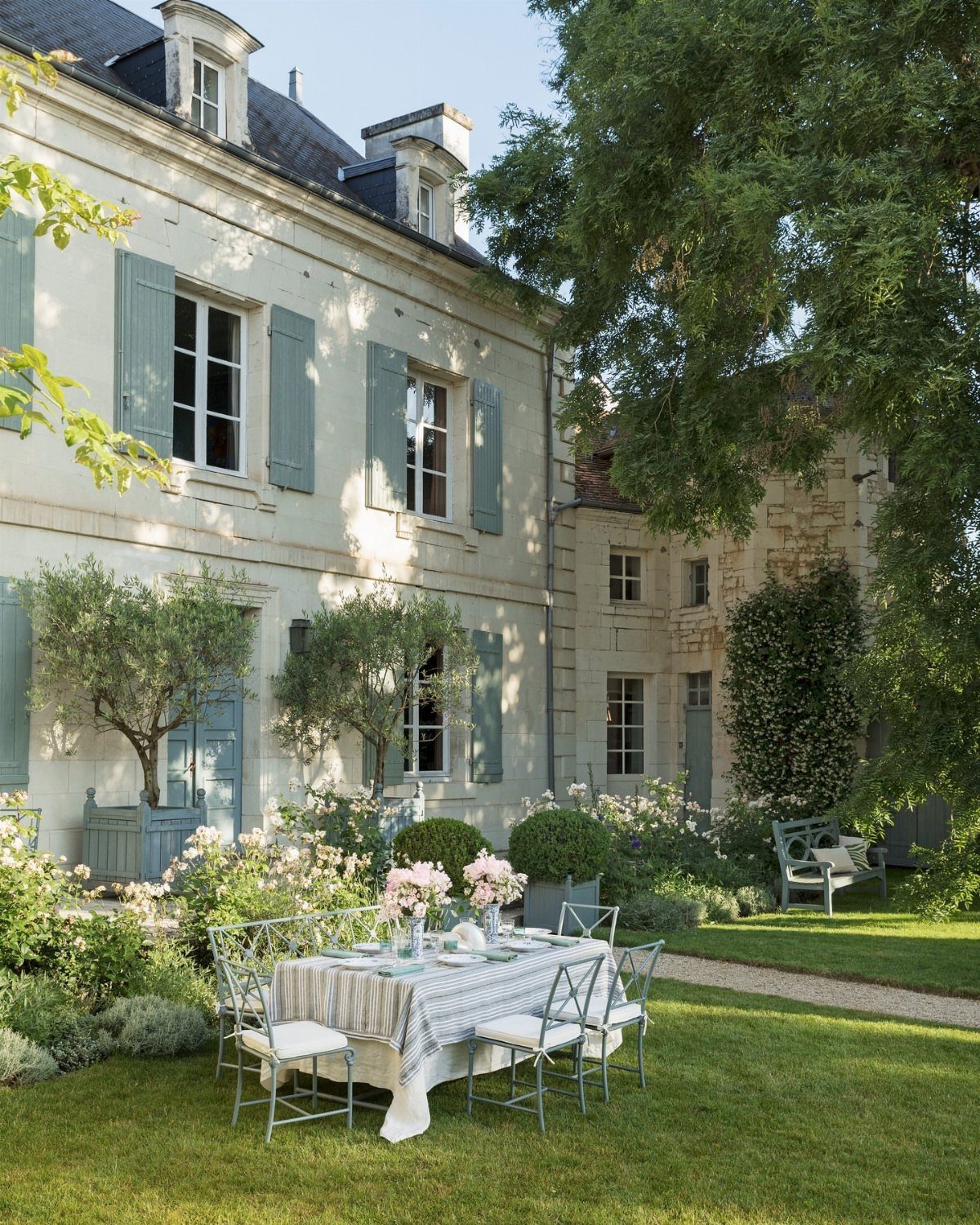 Dining table with floral centerpieces on a lawn before a French stone manor.