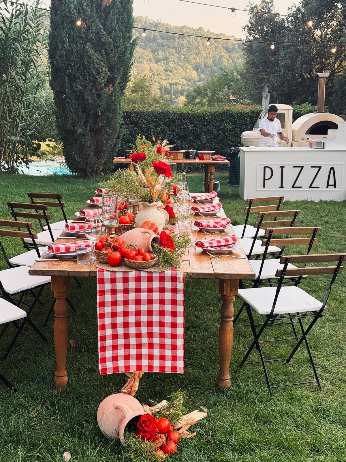 Outdoor dining table with red checkered linens and a pizza oven station.