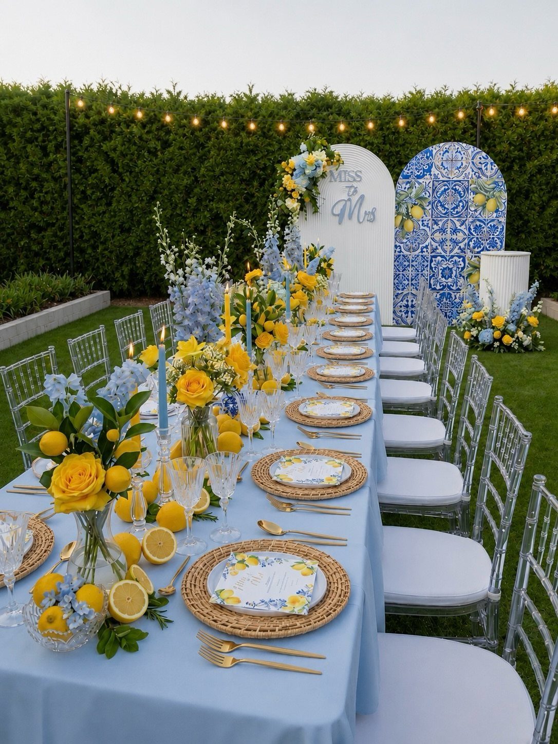 Outdoor dining table decorated with lemons, yellow roses, and blue accents on a lawn.